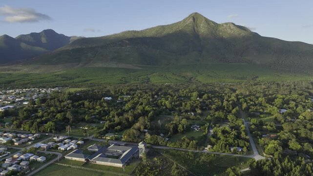 Drone orbits to the right around south side of a forested community at base of the Tsitsikamma Mountains at sunset in Stormsrivier, Eastern Cape, South Africa