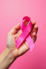Hand cradling pink ribbon against soft pink background, charity, disease, feminine