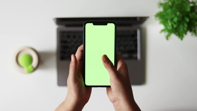 Woman sit use digital tech cell phone, green screen mock up. Hand scroll iphone web site, swipe like photos. Girl hold mobile closeup. Chroma key page. Cozy office background. Online app copy space.
