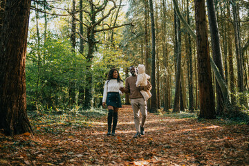 A family of three, a man and two women, are walking through a forest. The man is holding a baby in his arms. Scene is peaceful and serene, as the family enjoys their time together in nature