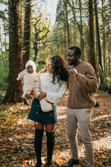 Fototapeta premium A man, a woman, and a baby are standing in a forest, with the baby being held by the woman. The man is smiling and he is happy. The scene is peaceful and serene