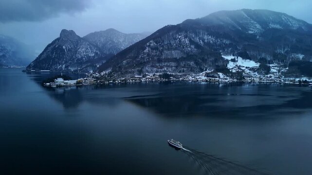 Aerial drone circling behind boat on Traunsee lake revealing alpine mountain winter landscape, Austria