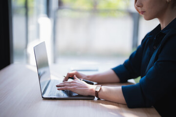 Woman focusing on her work, typing on a laptop computer while sitting at a light wooden desk, representing concepts of remote work, online learning, and technology use