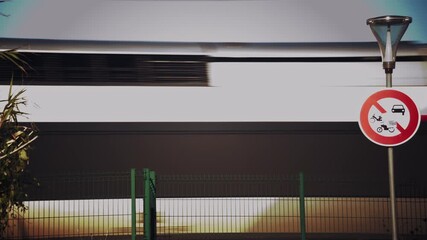 Side view of a passenger train moving past a green fence near the railway tracks