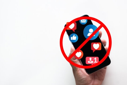 Hand holding smartphone with social media icons and red forbidden sign. Concept of digital detox, stopping internet addiction, social media ban, mental health awareness, and disconnection on white.