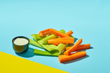 Raw carrot pieces and celery stalks with sauce on color background