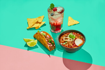 Mexican cuisine dishes, set meal of tacos, birria ramen soup, corn nachos chips and berry lemonade on colored background