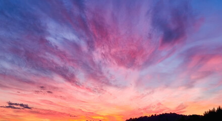 A vibrant sunset sky with hues of pink, orange, purple and blue clouds radiating out from the horizon