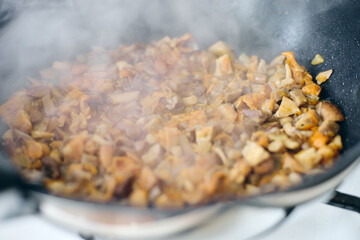 Finely chopped chanterelles, oyster mushrooms and champignons are fried in frying pan. Cooking process.