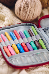Set of crochet hooks with multi-colored handles in an organizer and balls of yarn in natural colors on white knitted background.