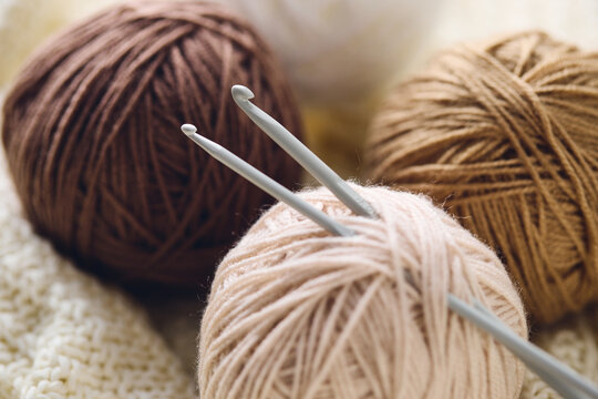 Crochet hooks and balls of beige and brown yarn on white knitted background. Knitting, crocheting supplies.