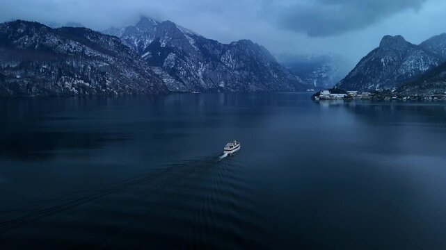 Aerial drone flying left to right following boat on Traunsee lake with foggy mountain landscape, Austria