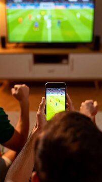 Soccer fans watching match on smartphone and television simultaneously while celebrating at home