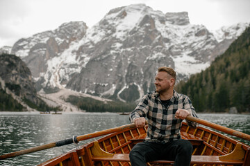 Man rowing wooden boat on Braies Lake with snowy mountains in background