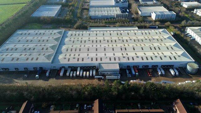Milton Keynes, United Kingdom - 20 December 2025: Aerial view of delivery trucks lined up at a vast warehouse with a grey roof and loading bays.