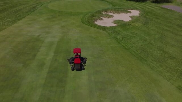 Boston, United States - 26 December 2025: Aerial view of a red mower traversing lush green golf course near a sand trap, revealing textures and tones.