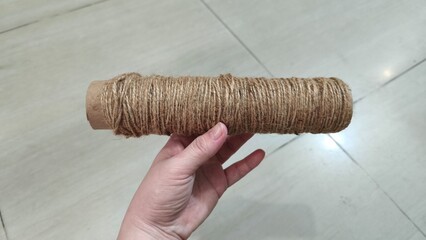 Hand holding a cardboard tube wrapped with natural twine for crafting projects