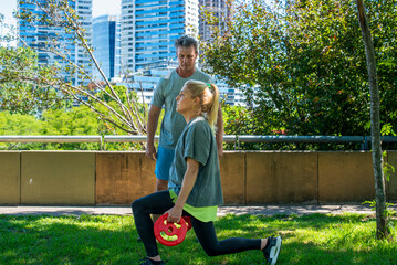Middle aged couple training with weight plate in a sunny urban park