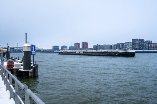 Dordrecht Netherlands - 5 January 2026: Winter harbour with gas cargo barge passing Dordrecht on a calm, snowy urban industrial waterfront maritime transport scene on theMaas River in the Netherlands.