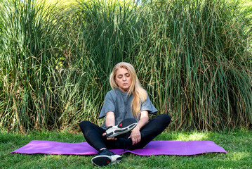 Sporty female sitting on a mat and removing her shoes before meditating outdoors