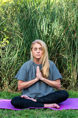 Blonde woman in prayer pose practicing outdoor meditation on a sunny day