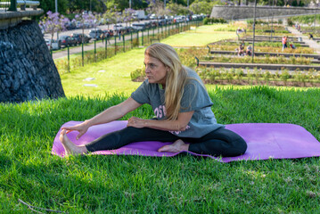 Middle aged woman performing seated leg stretches on a yoga mat outdoors