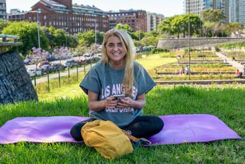 Smiling woman using her smartphone while resting on a yoga mat in an urban park