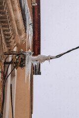 Icicles forming on electrical cables attached to a building facade during winter snowfall, highlighting frozen urban infrastructure, cold weather hazards and climate conditions.