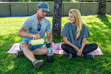Fit woman and man in sportswear taking a break to drink mate in nature