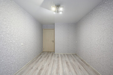 Fototapeta premium Empty room with light grey textured wallpaper, light wood laminate floor, white ceiling, modern ceiling light fixture, light wooden door, minimalistic design
