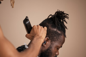 A barber trims and blends the side fade of a male client’s haircut using electric clippers. The close-up highlights textured hair, precise clipper work, and modern men’s grooming in a studio 