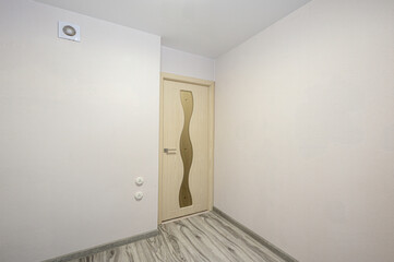 Minimalist room with light grey laminate floor, off-white walls, light wooden door with wavy glass...