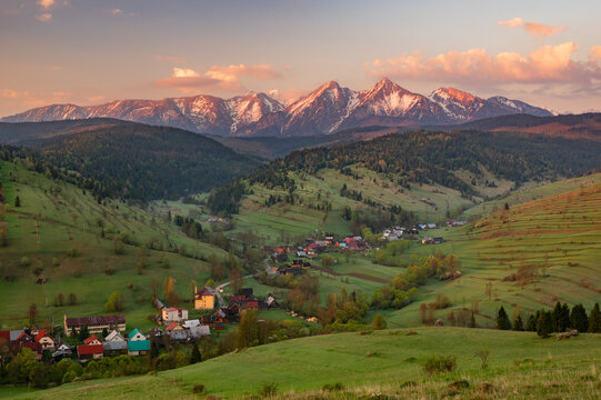 Aerial view of a verdant valley cradling quaint villages beneath the majestic, snow-capped Tatra Mountains, kissed by the soft hues of dawn, Osturna, Presov Region, Slovakia.
