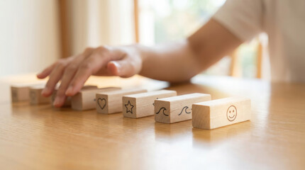 A persons hand reaches for wooden blocks stacked on a table near a window with light coming through the sheer curtains