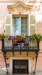 A charming building facade featuring a decorative balcony with flowers, a table, and chairs.