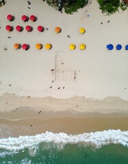 An aerial view captures a vibrant beach scene with colorful umbrellas, a volleyball court, and ocean waves.
