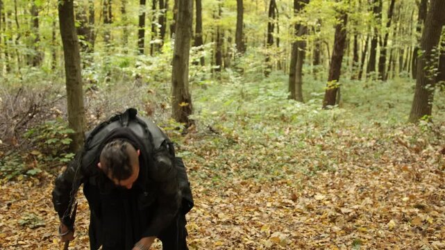 Splitting logs, Dark ensemble, Bearded warrior. Clad in dark clothing, bearded Viking is chopping wood with axe in autumnal woodland.