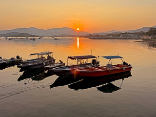 Serene sunset over calm water with moored boats and distant mountain