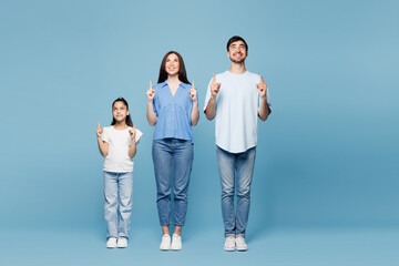 Fototapeta premium Full body young happy fun parents mom dad with child kid daughter girl wearing casual clothes point index finger overhead on blank area isolated on plain blue background. Family day childhood concept.