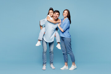 Full body young fun happy parents mom dad with child kid daughter girl wear casual clothes giving piggyback ride to joyful, sit on back isolated on plain blue background. Family day childhood concept.