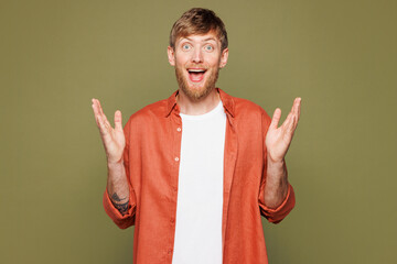 Shocked happy young blond man he wearing basic white t-shirt orange shirt keeping mouth open spreading hands surprised look camera isolated on plain pastel green color wall background studio portrait.