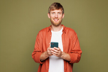 Young smiling cheerful happy man he wears basic white t-shirt orange shirt look camera hold in hand use mobile cell phone isolated on plain pastel green background studio portrait. Lifestyle concept.