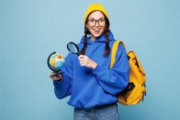 Young overjoyed happy smart traveler woman student she wear glasses casual clothes yellow backpack bag hold globe isolated on pastel plain light blue color background. High college lifestyle concept.