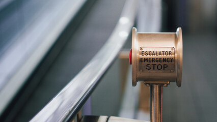 Escalator emergency stop button with metallic railing and blurred background
