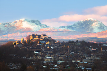 Epic winter landscape and cityscape view of Stirling Castle at sunset with mountain backdrop and peaks of Stuc a'Chroin and Ben Vorlich in the Scottish Highlands of Scotland, UK.