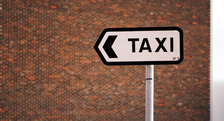 Directional taxi sign pointing left against textured brick wall