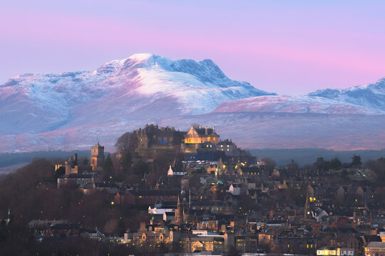 Epic winter landscape and cityscape view of Stirling Castle at twilight with mountain backdrop and peaks of Stuc a'Chroin and Ben Vorlich in the Scottish Highlands of Scotland, UK.