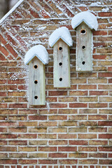 Three snow-covered wooden birdhouses adorn a rustic brick wall, showcasing a charming winter scene with intricate brickwork and frosty details.