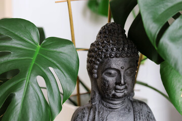 Close-up of black, ceramic budda statue hidden among big monsterra leaves