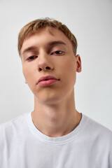 Fototapeta premium Close up of a young man with a neutral background, wearing a white t shirt, and a relaxed expression, captured in a minimal studio setting for fashion and lifestyle projects